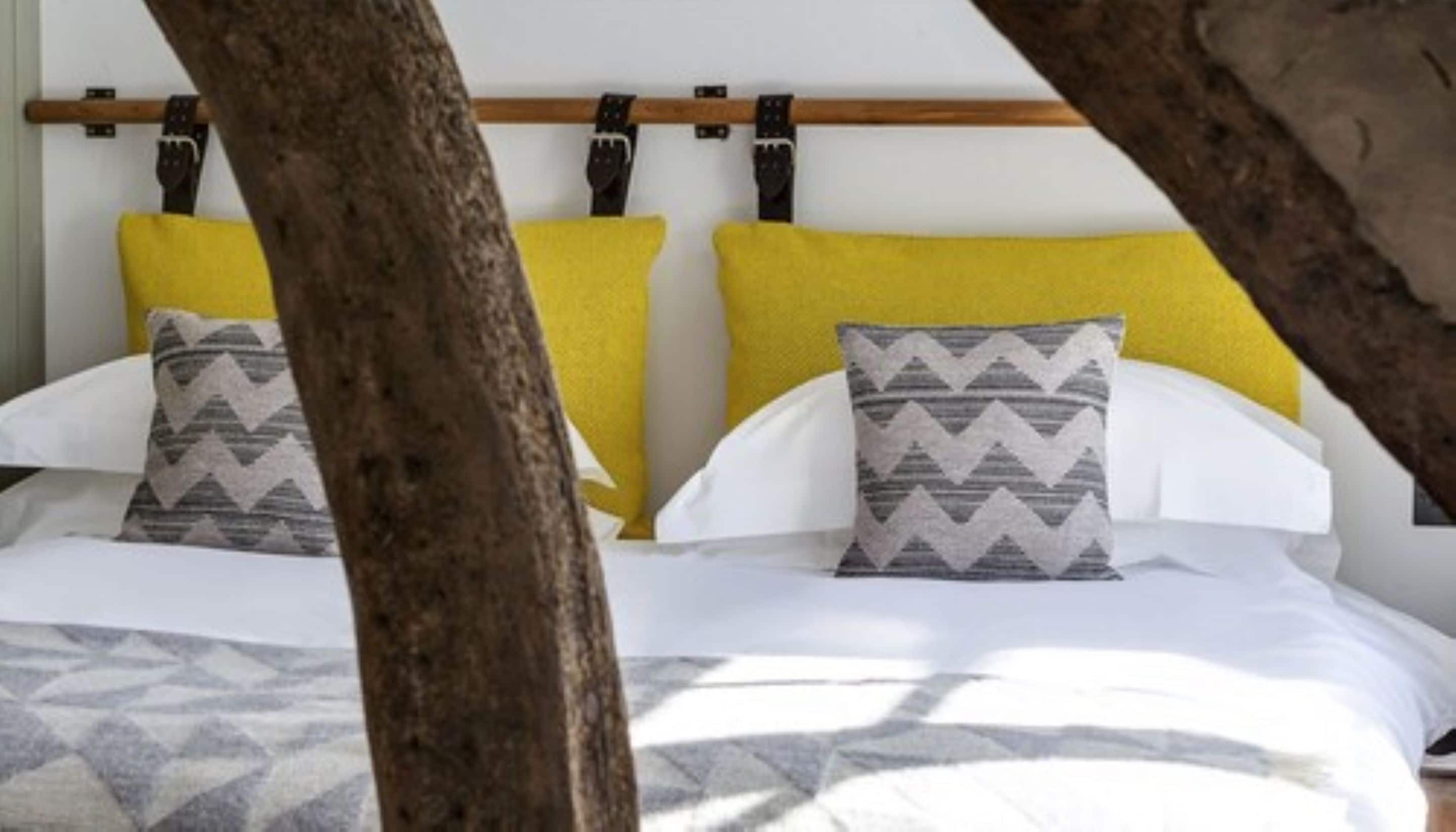 A bed with white bedding and two pillows, one with a zigzag pattern and the other plain.
