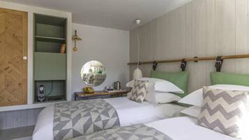 A bedroom with two beds, a wooden wardrobe, a mirror, and a bedside table with a lamp.