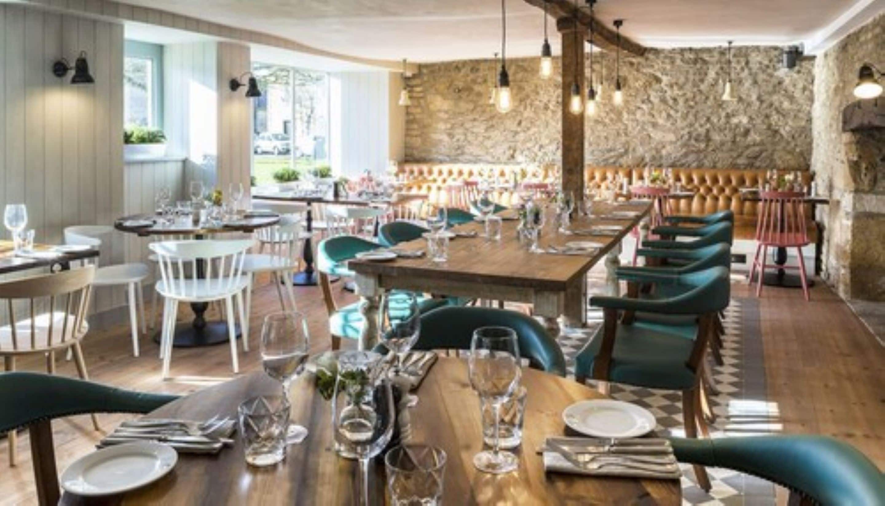 Ein Restaurant mit Holztischen und -stühlen, Steinwänden und hängenden Lampen.