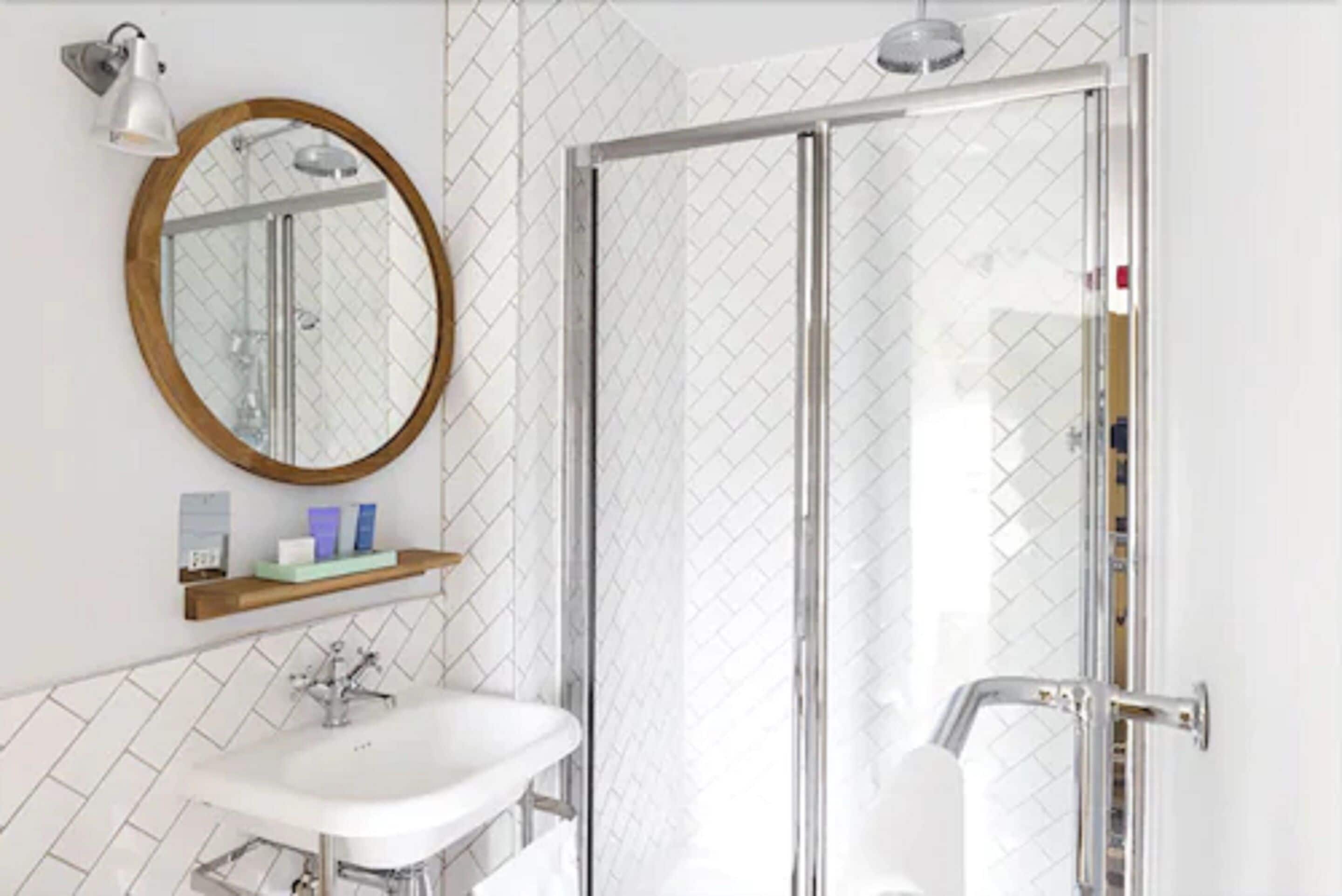 Une salle de bain moderne avec une douche à l’italienne en verre, un miroir rond et un lavabo blanc.