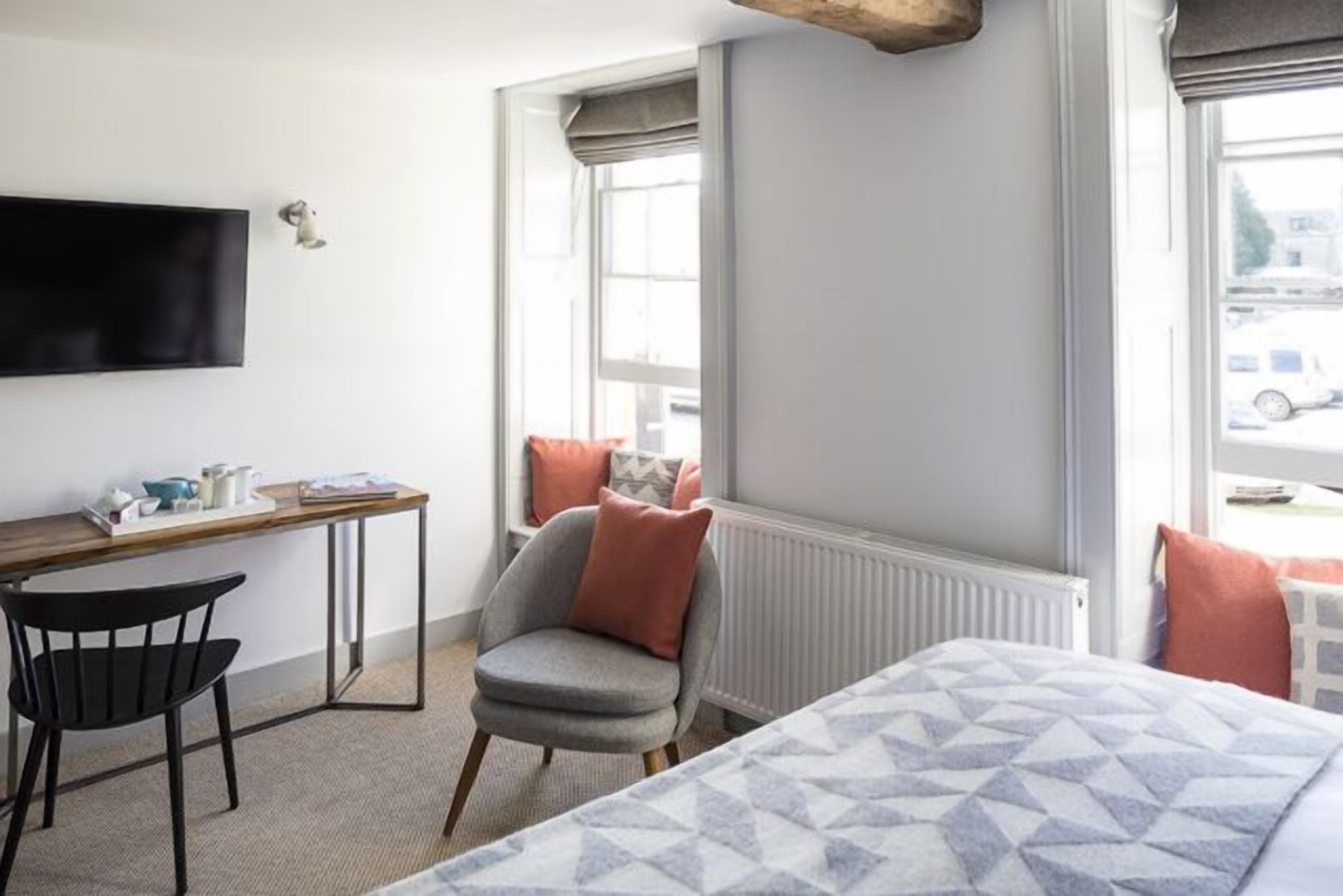 A hotel room with a bed, a desk, a chair, and a window with a view of the street.