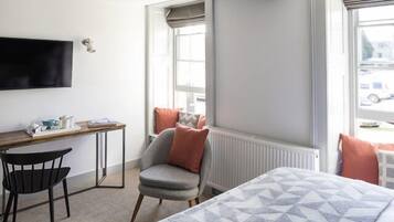 A hotel room with a bed, a desk, a chair, and a window with a view of the street.