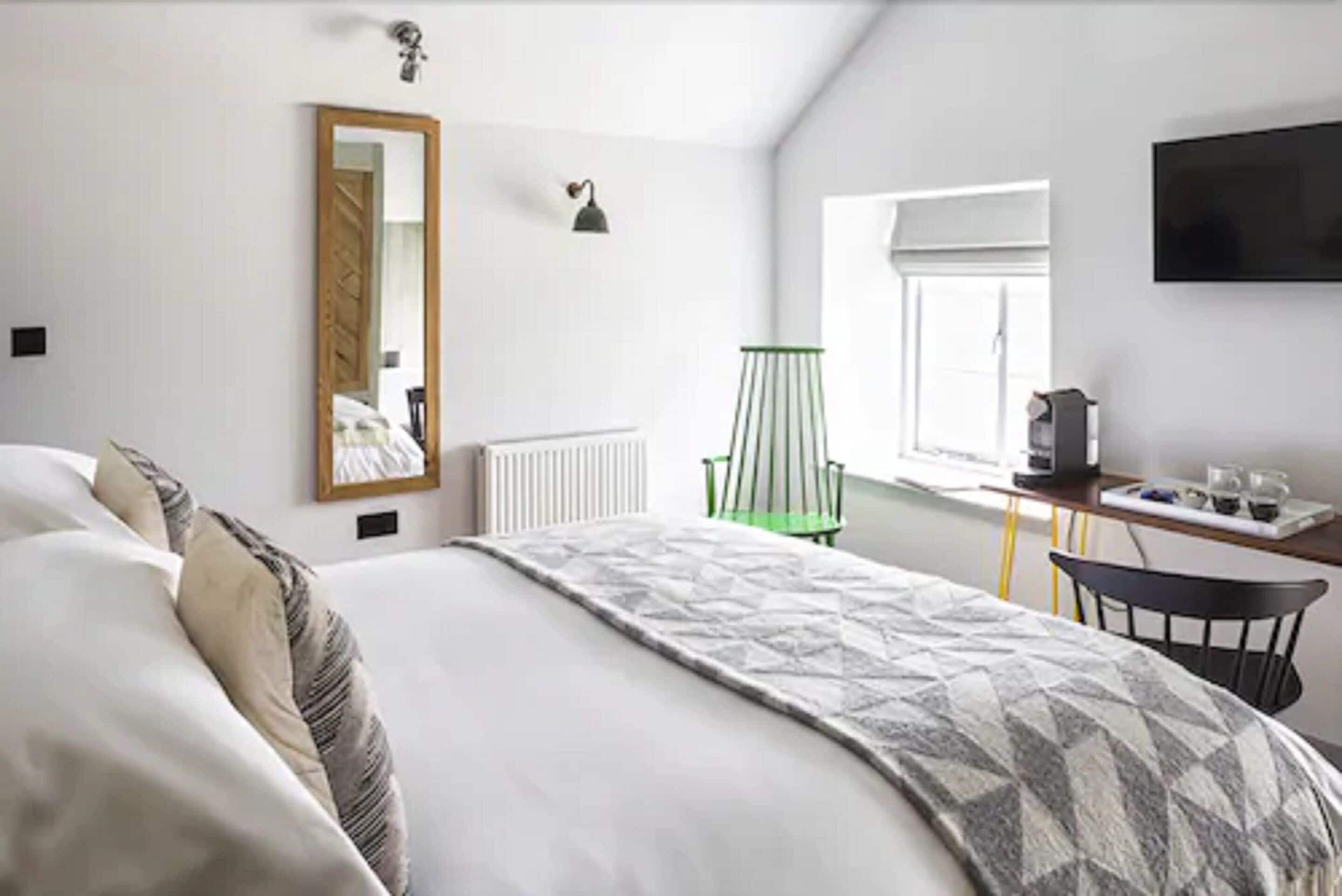A bedroom with a bed, a desk, a chair, a radiator, a mirror, a lamp, and a TV.