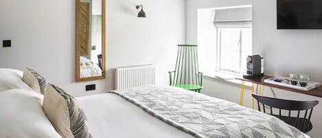 A bedroom with a bed, a desk, a chair, a radiator, a mirror, a lamp, and a TV.
