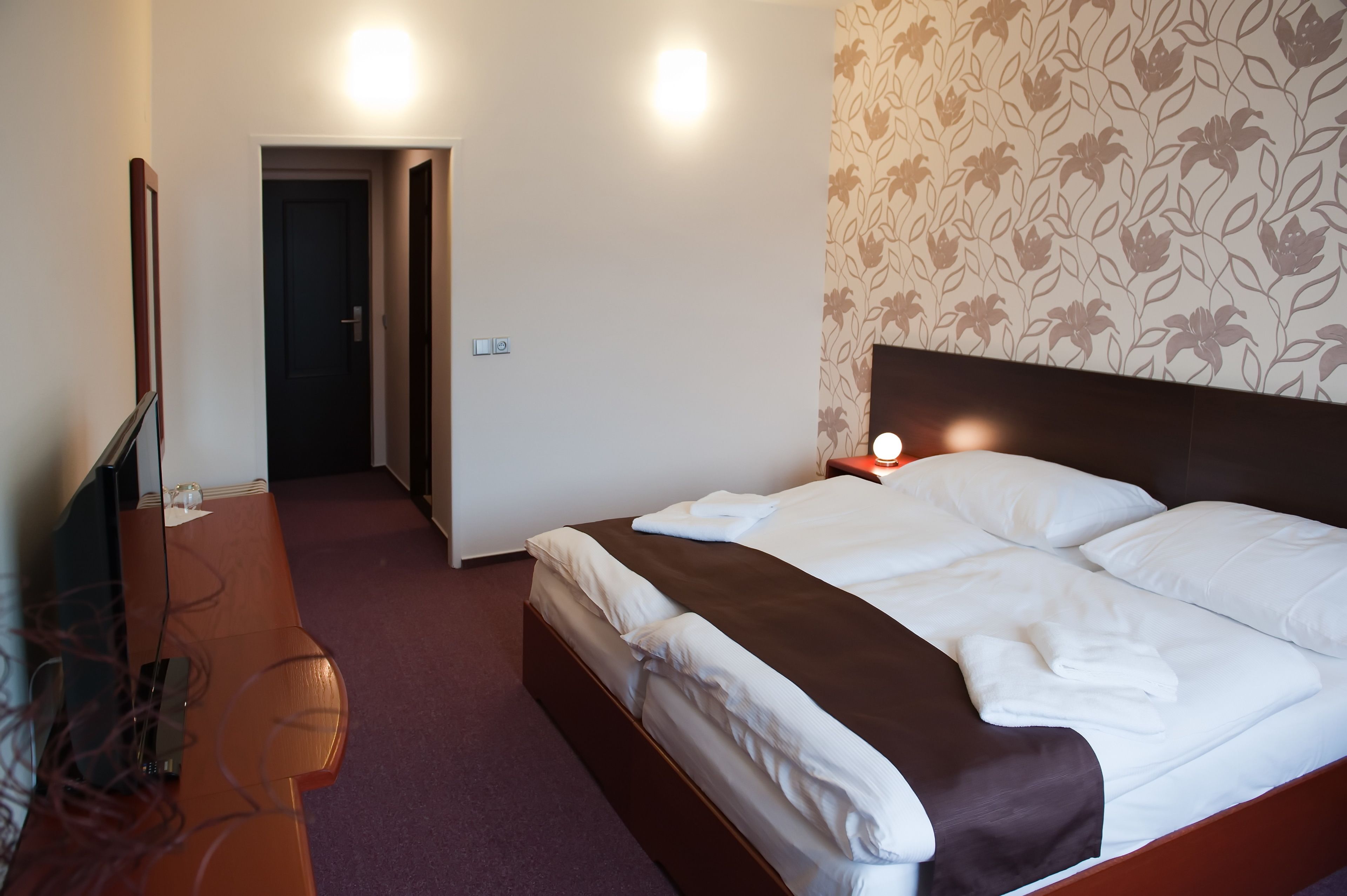 Quarto de hotel com uma cama, uma escrivaninha e uma televisão.