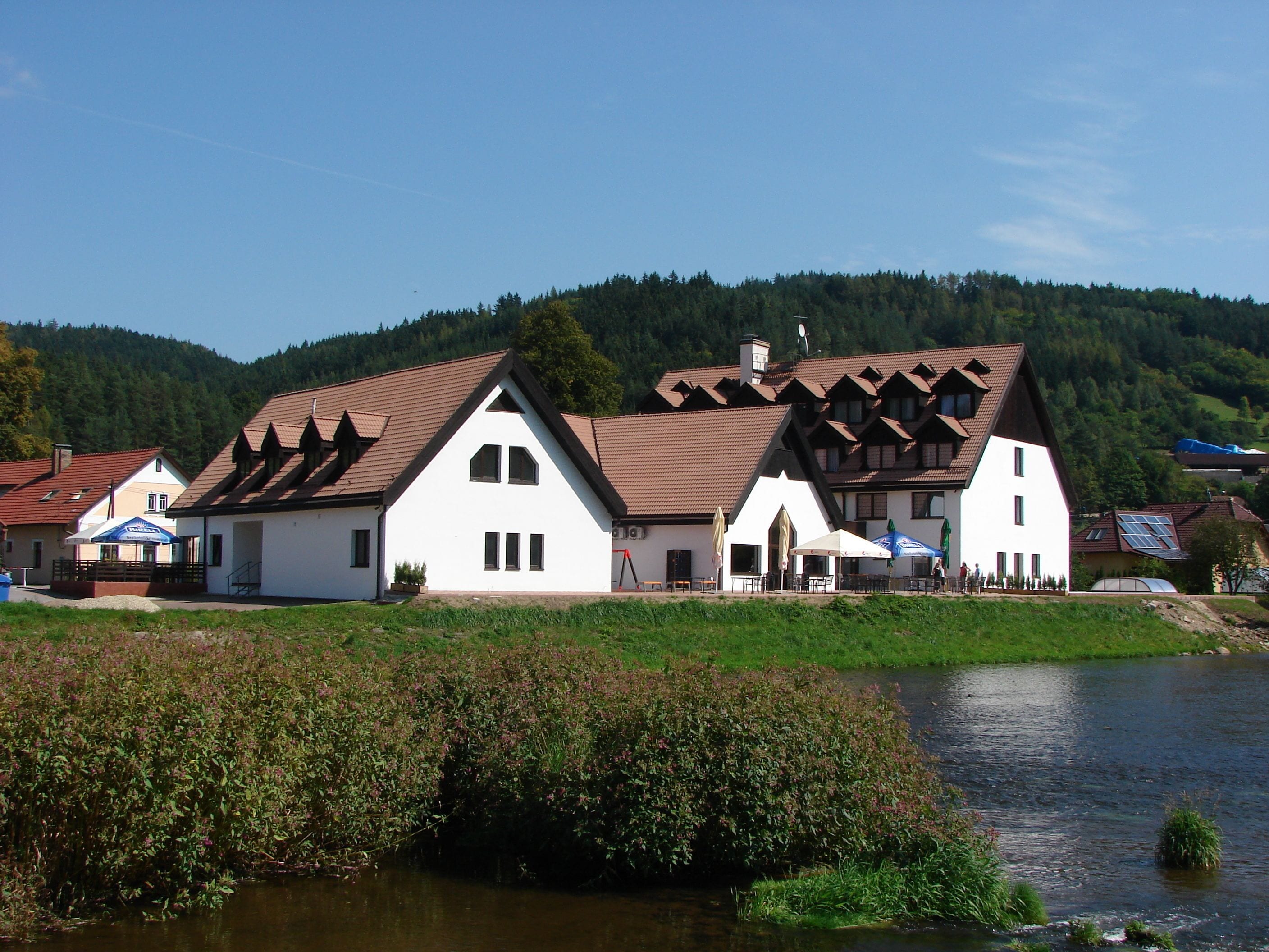 Ein traditionelles Gebäude mit einem geneigten Dach, einer kleinen Veranda und einem Fluss im Vordergrund.