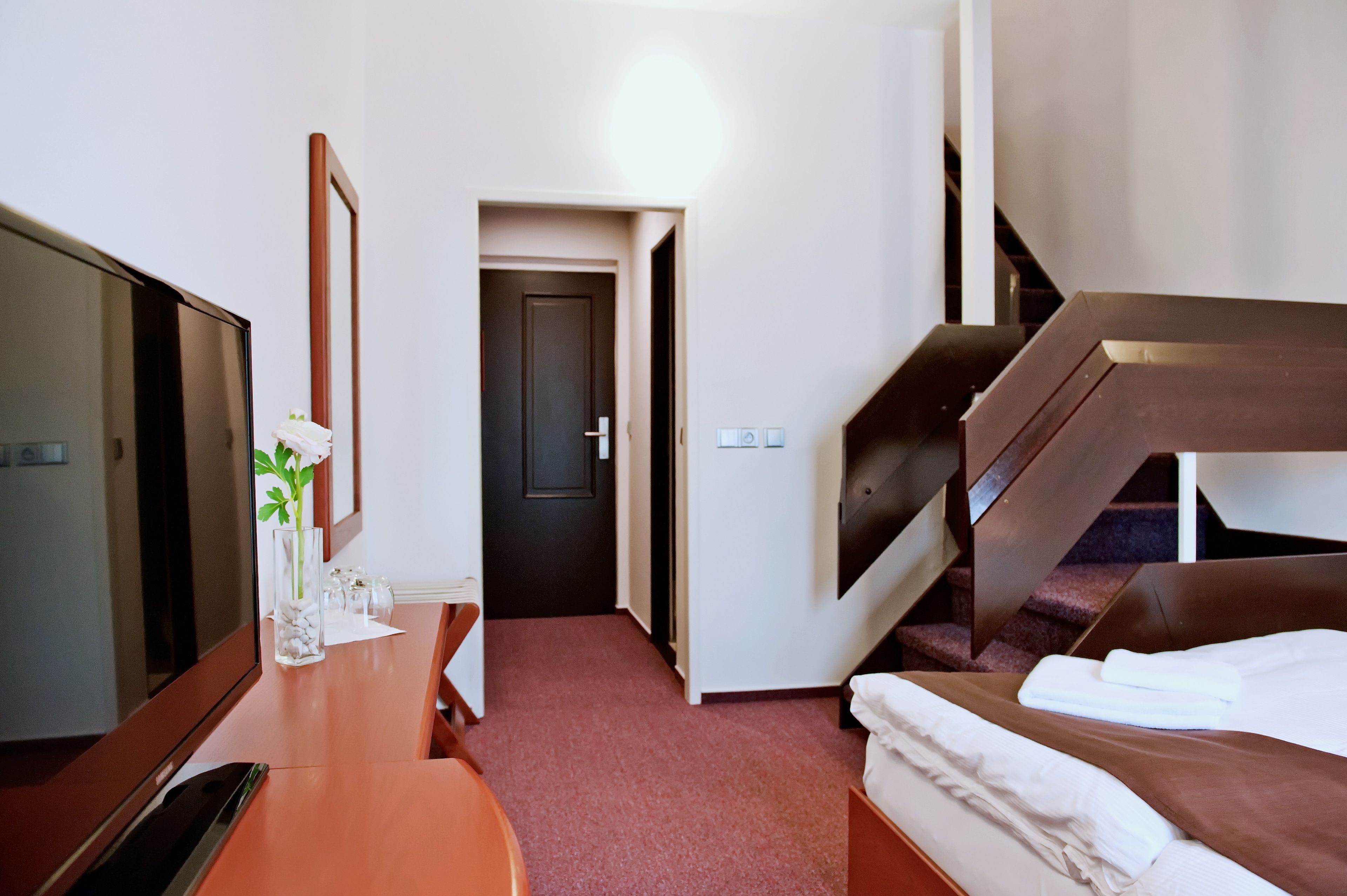 A hotel room with a bed, a desk with a TV, a mirror, and a staircase.