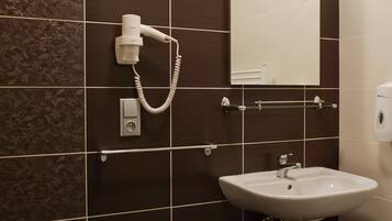 A bathroom with dark brown tiles, a white sink, a mirror, and a hairdryer mounted on the wall.