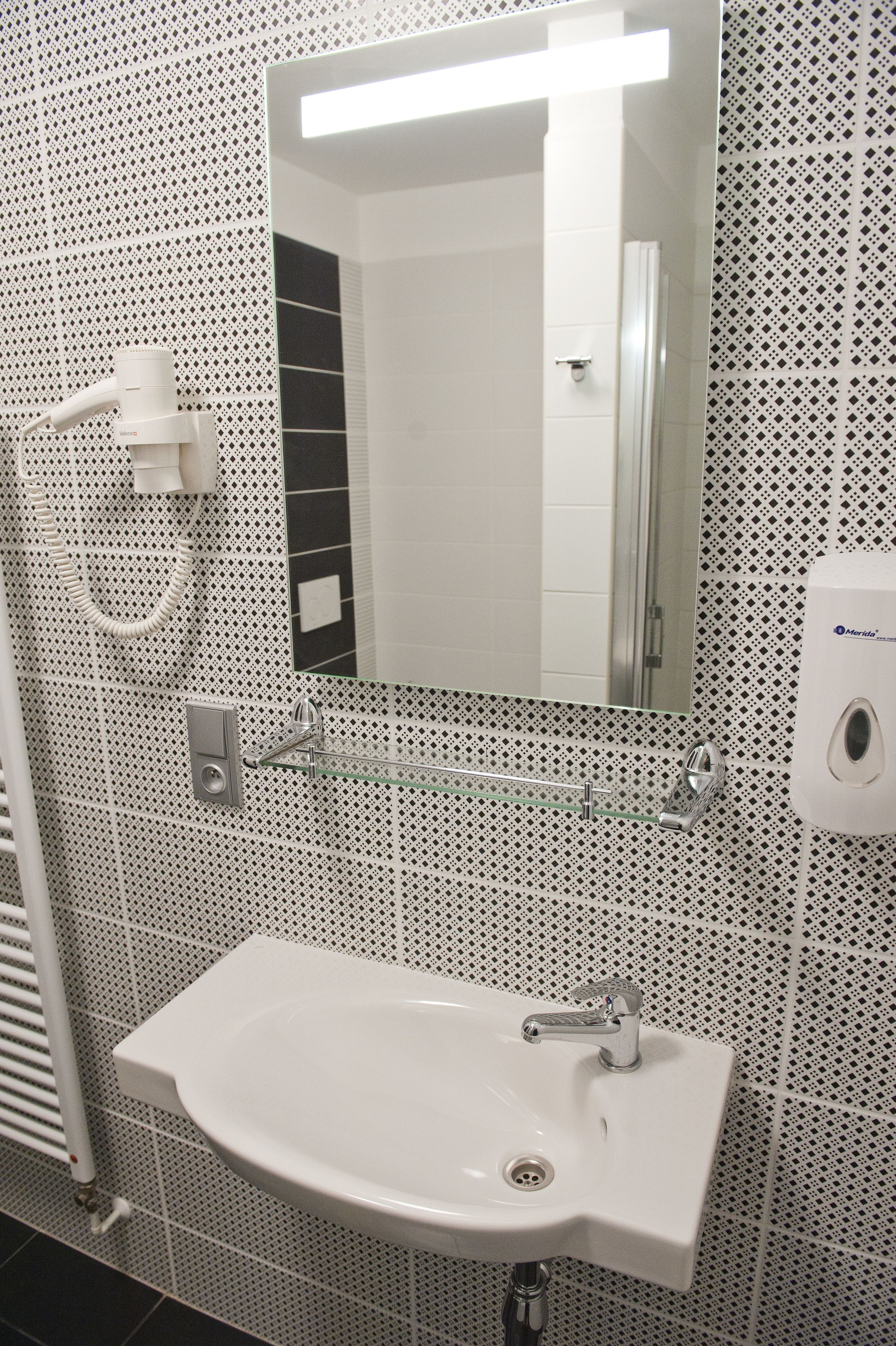 Un baño con un lavabo blanco, un espejo y un secamanos.