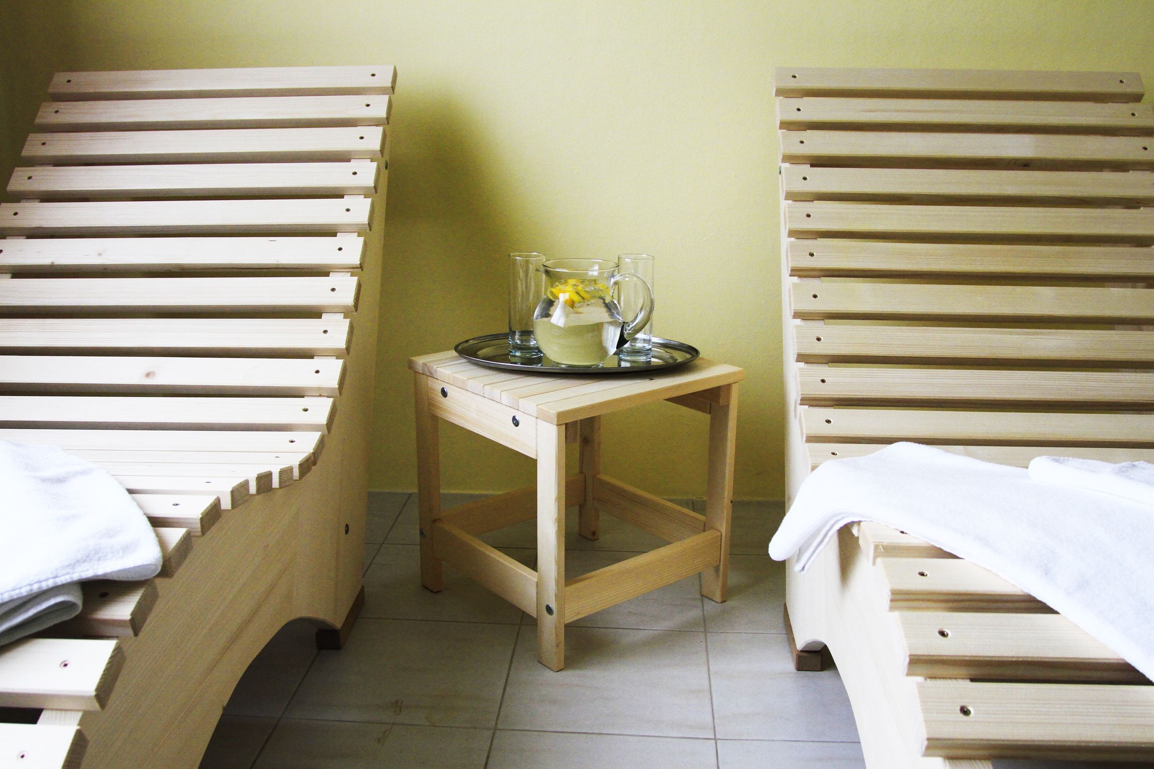 Una habitación con dos camas de madera, una mesita de madera con una bandeja que sostiene un vaso de agua y un limón, y una pared lisa.