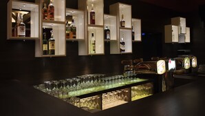 A bar area with multiple shelves displaying bottles of liquor, a bar counter with glasses, and a beer tap. - Hotel Vír (Vir)