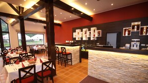 A restaurant with a stone bar, red chairs, and tables set for dining. - Hotel Vír (Vir)
