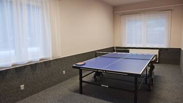 A ping pong table in a room with carpeted floors and a window with sheer curtains.
