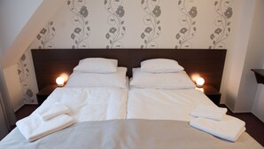 A neatly made double bed with white linens and a grey throw blanket, two bedside lamps, and a floral wallpaper pattern on the wall. - Hotel Vír (Vir)