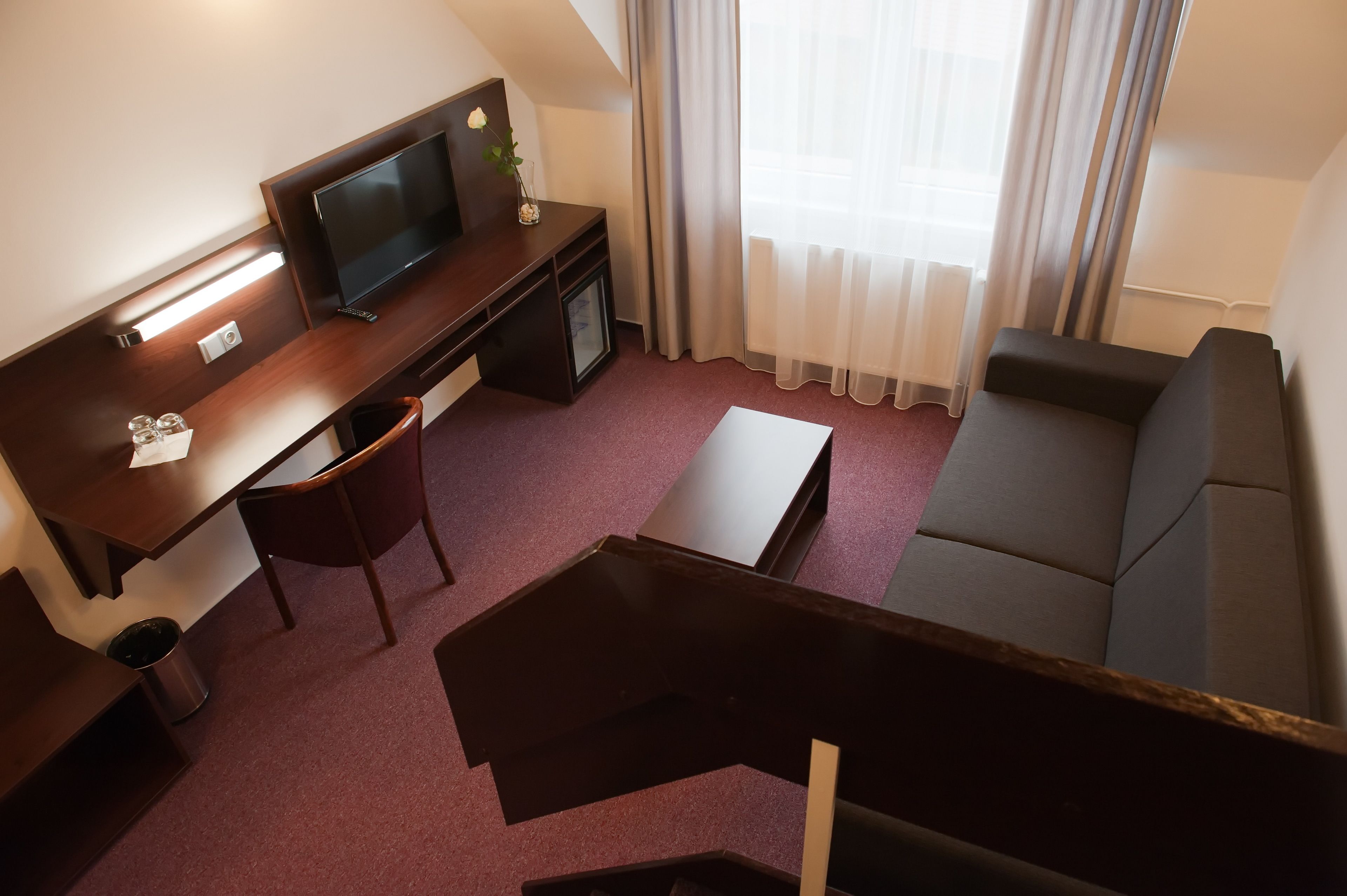 A hotel room with a desk, chair, sofa, TV, and a small table.