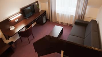 A hotel room with a desk, chair, sofa, TV, and a small table.