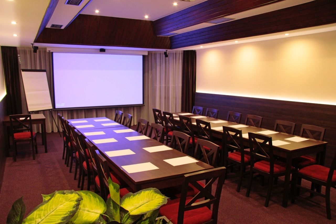 A conference room with a large screen, multiple tables, and chairs.