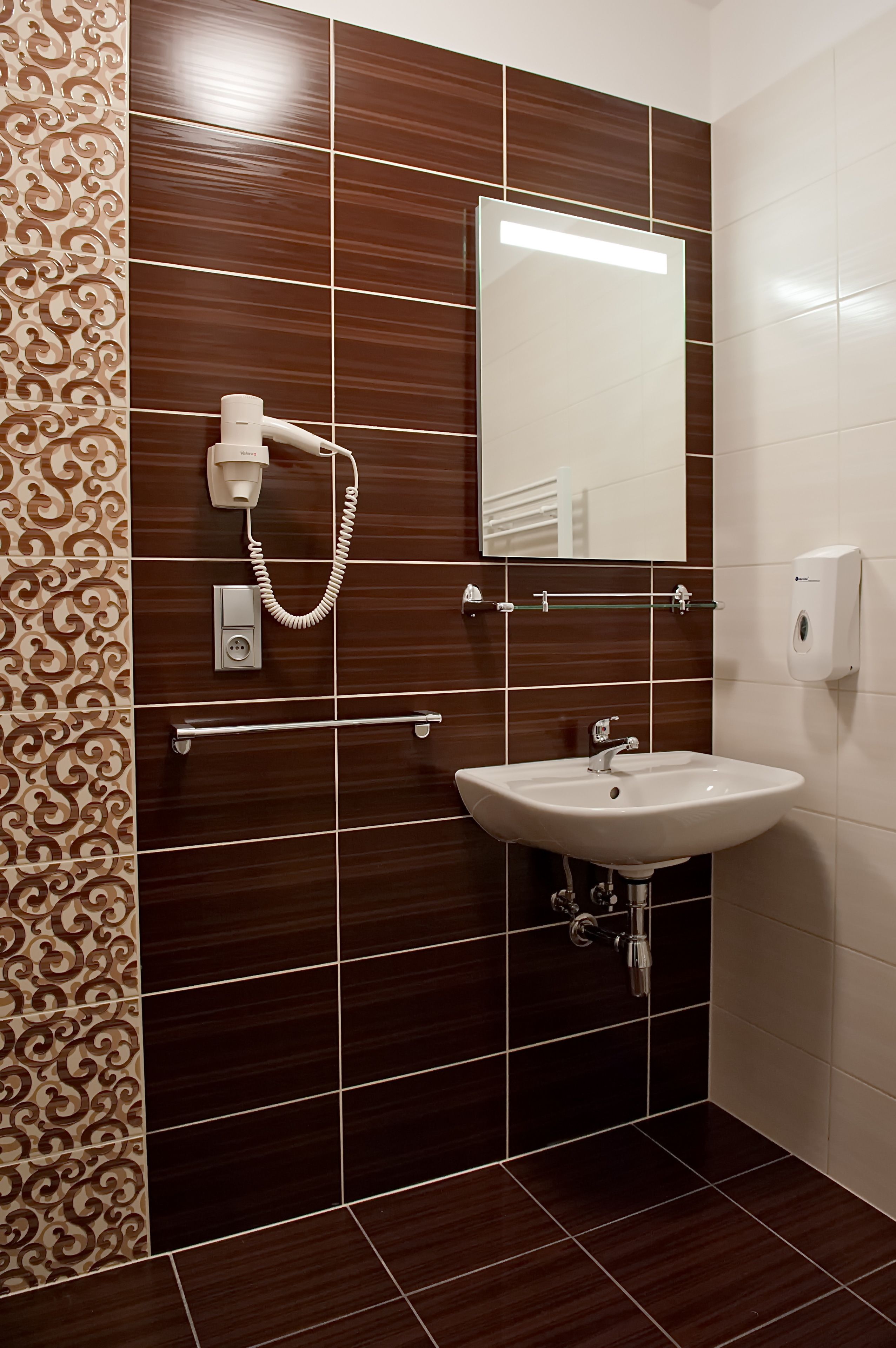 Une salle de bain avec un lavabo blanc, un miroir, un sèche-cheveux et un distributeur de savon.