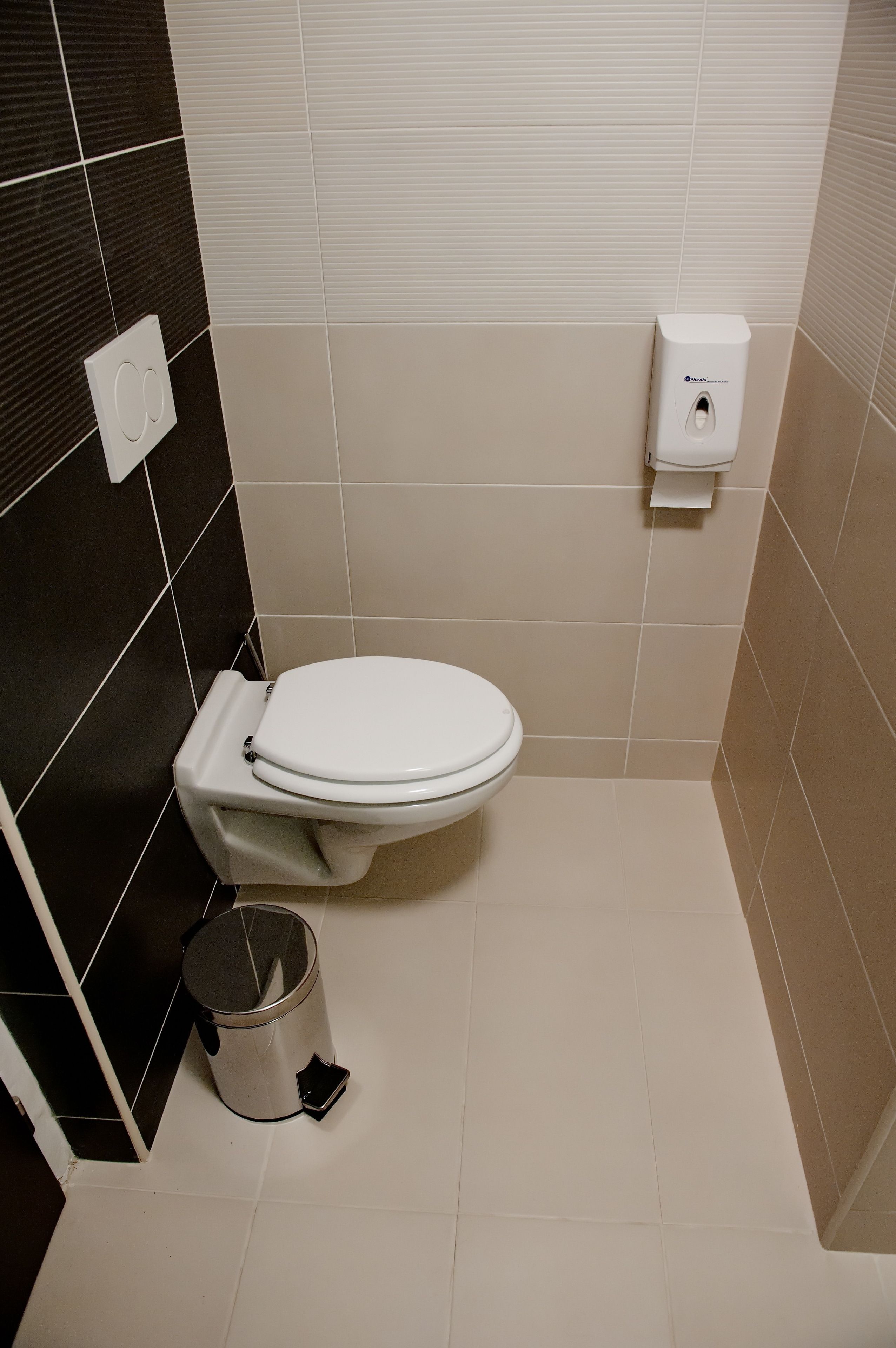 Um banheiro pequeno e moderno, com vaso sanitário branco, lixeira e dispensador de papel higiênico.