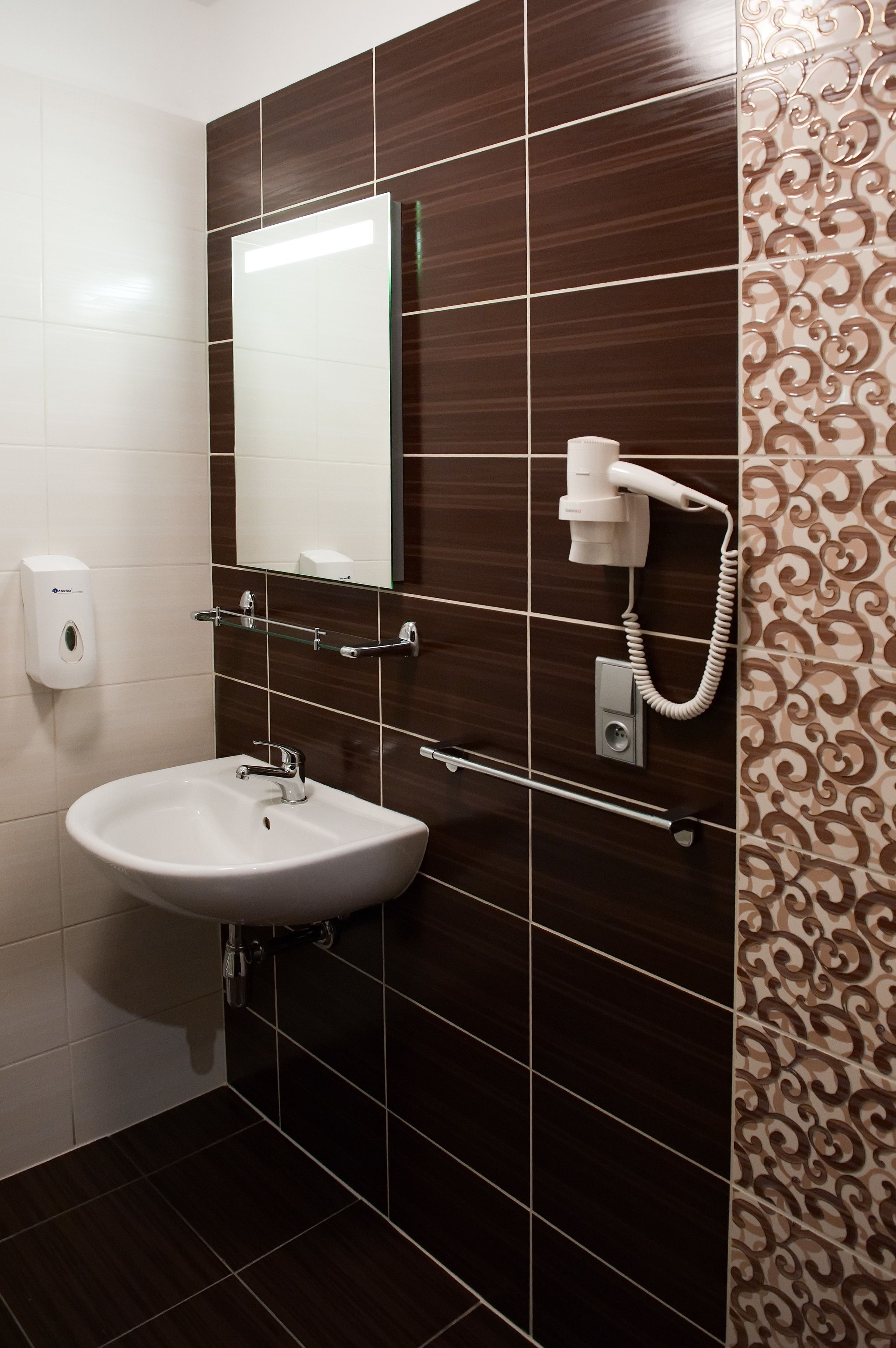 Une salle de bain avec un lavabo blanc, un miroir et un sèche-cheveux fixé au mur.