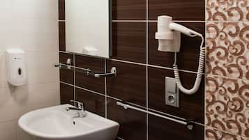 Une salle de bain avec un lavabo blanc, un miroir et un sèche-cheveux fixé au mur.