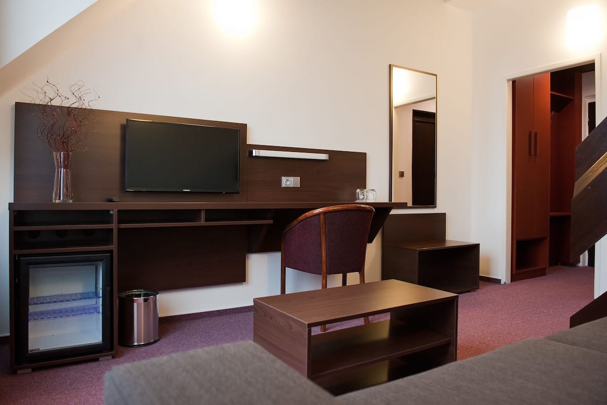 Una habitación de hotel moderna con televisión de pantalla plana, un escritorio de madera, una silla, una mesita, un bote de basura y un armario.