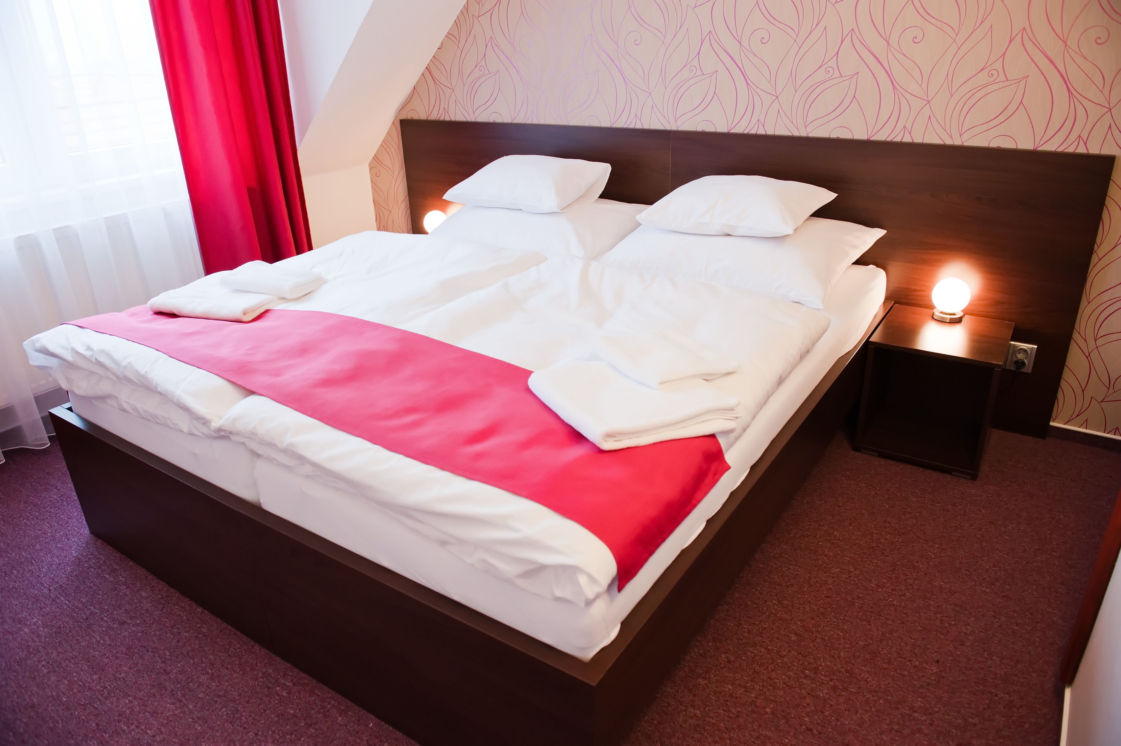 A neatly made bed with white and red bedding, a wooden headboard, and bedside lamps.