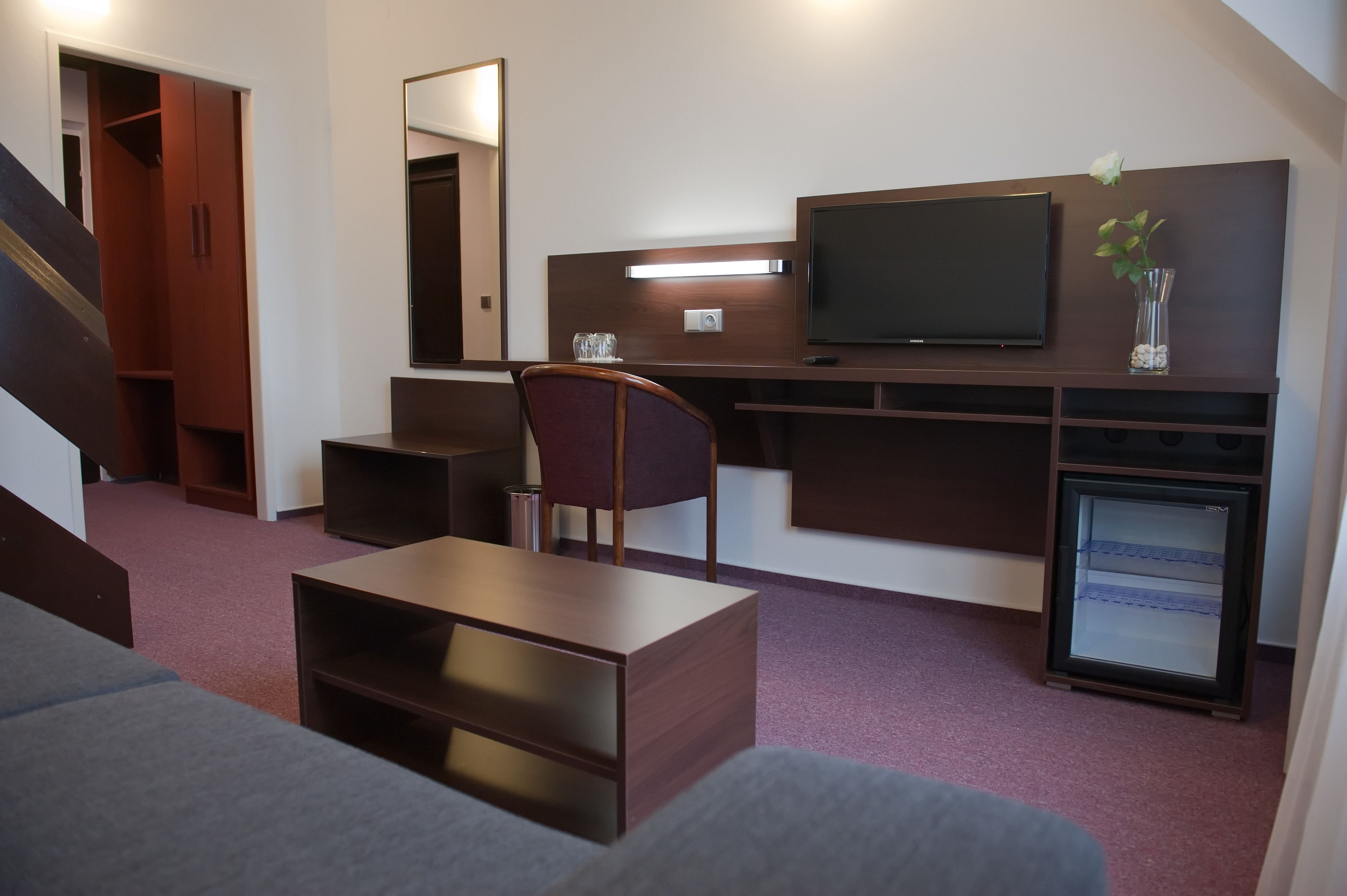 Ein Hotelzimmer mit einer Couch, einem Schreibtisch, einem Stuhl, einem Fernseher, einer kleinen Kühlschrank und einem Spiegel.