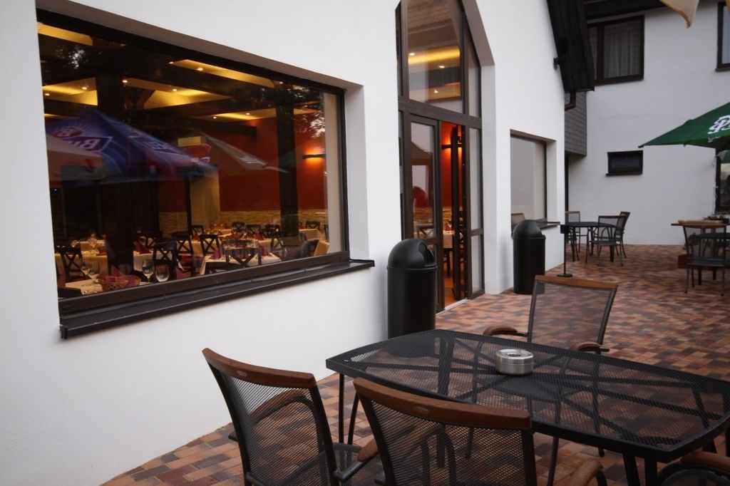 An outdoor patio area with tables and chairs, a window with a view of the interior, and a green umbrella.