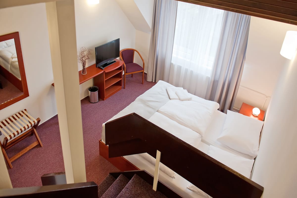 Habitación de hotel con cama, televisor, silla, escritorio y escalera.