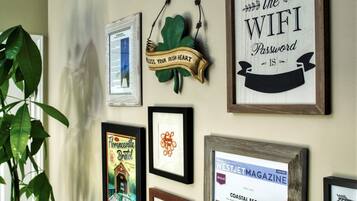 A wall with various framed items, including a sign that says "WELCOME the WIFI Password is" and a framed magazine cover.