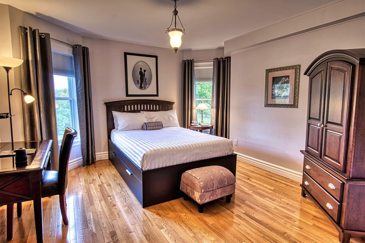 Ein Schlafzimmer mit einem großen Bett, einem Holztisch, einem Stuhl, einer Kommode und einem Fenster mit Vorhängen.