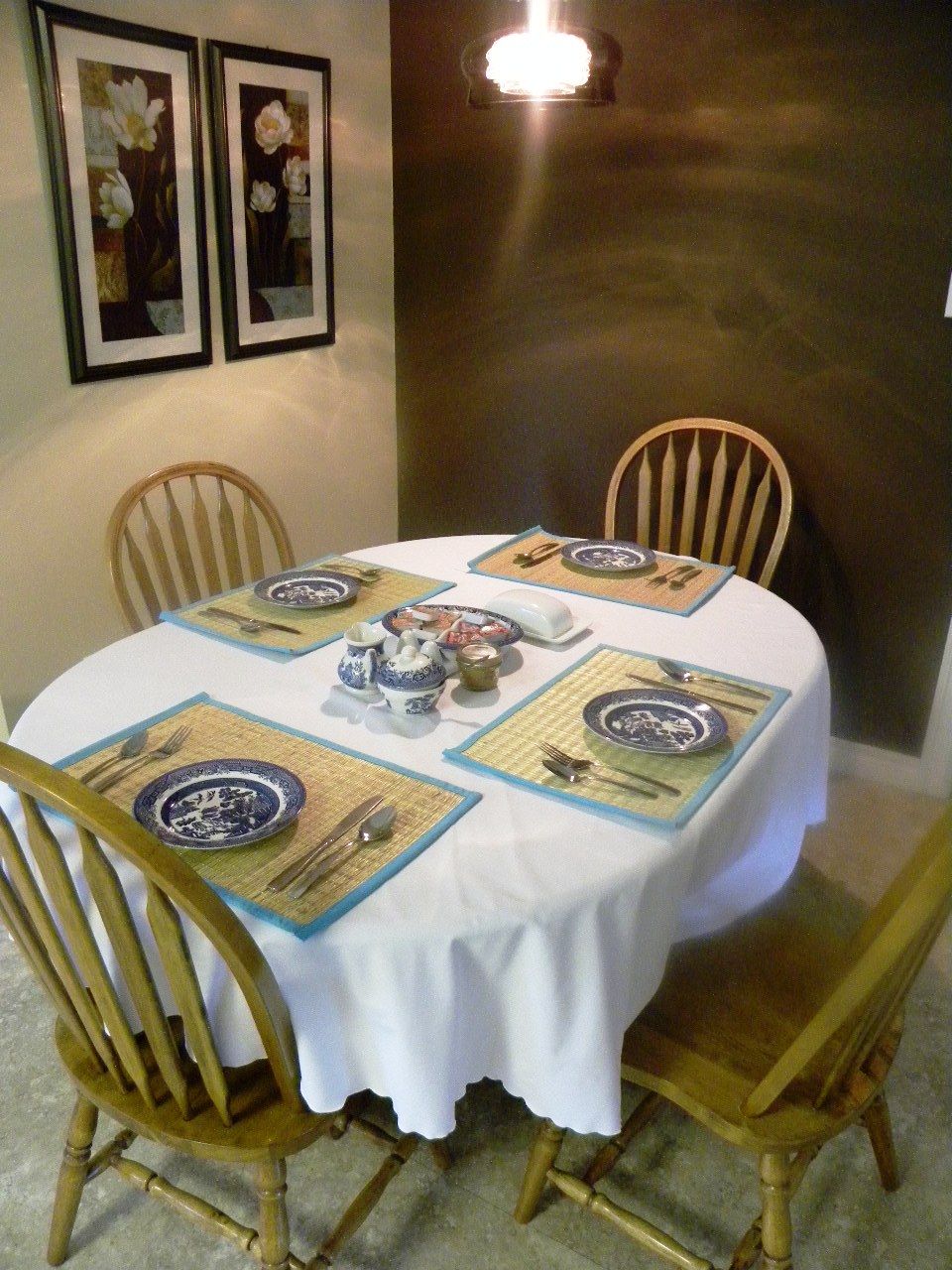 Un tavolo rotondo da pranzo con tovaglia bianca, quattro sedie e un servizio di piatti bianchi e blu con posate coordinate.