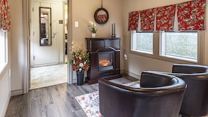 A living room with a fireplace, dark leather chairs, a patterned rug, and a window with red floral curtains. - Shamrock Suites (Florenceville-Bristol)
