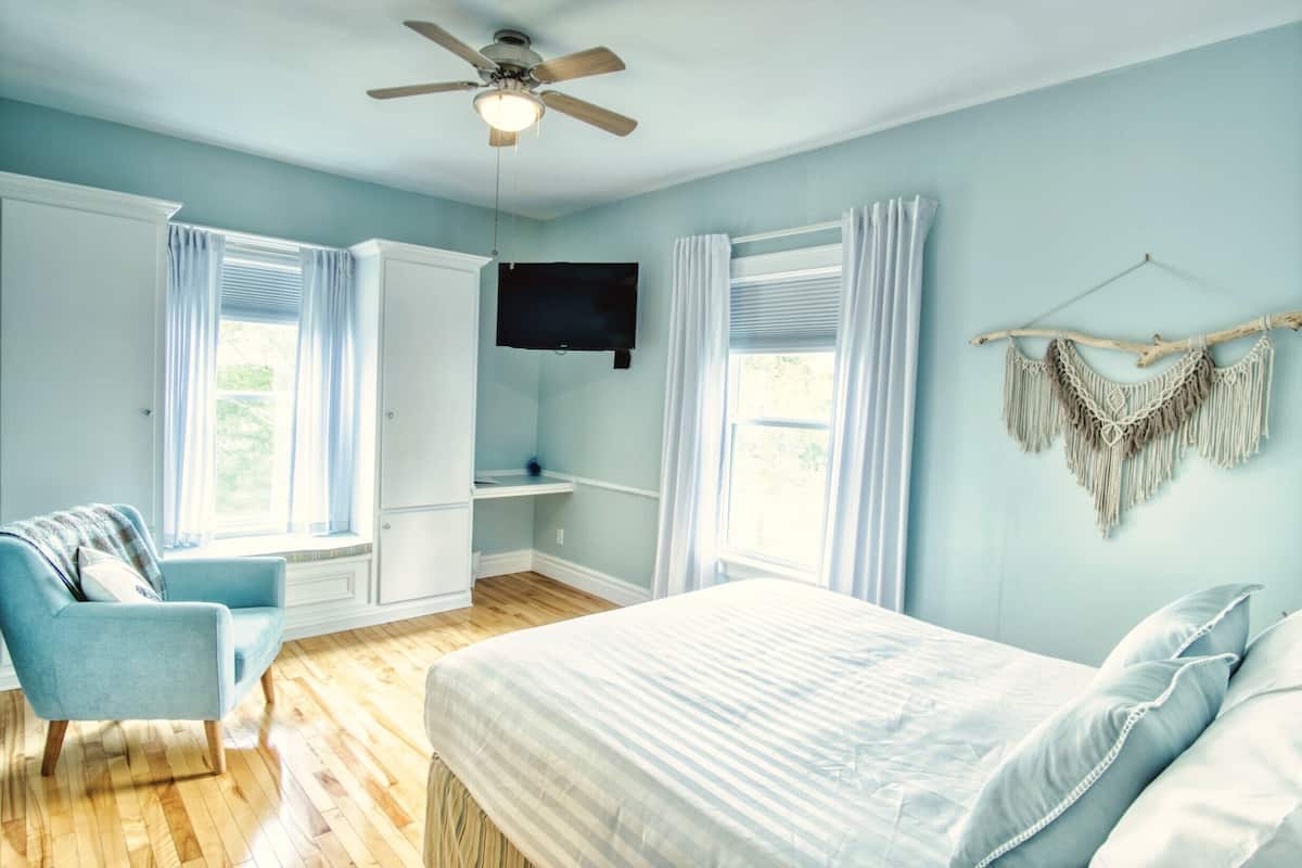 Ein Schlafzimmer mit Bett, Stuhl, Kleiderschrank, Fernseher und Deckenventilator.