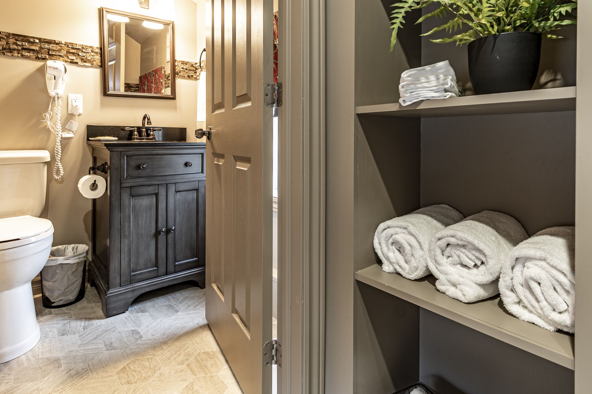 A bathroom with a toilet, a sink, a cabinet, and a shelf with towels.
