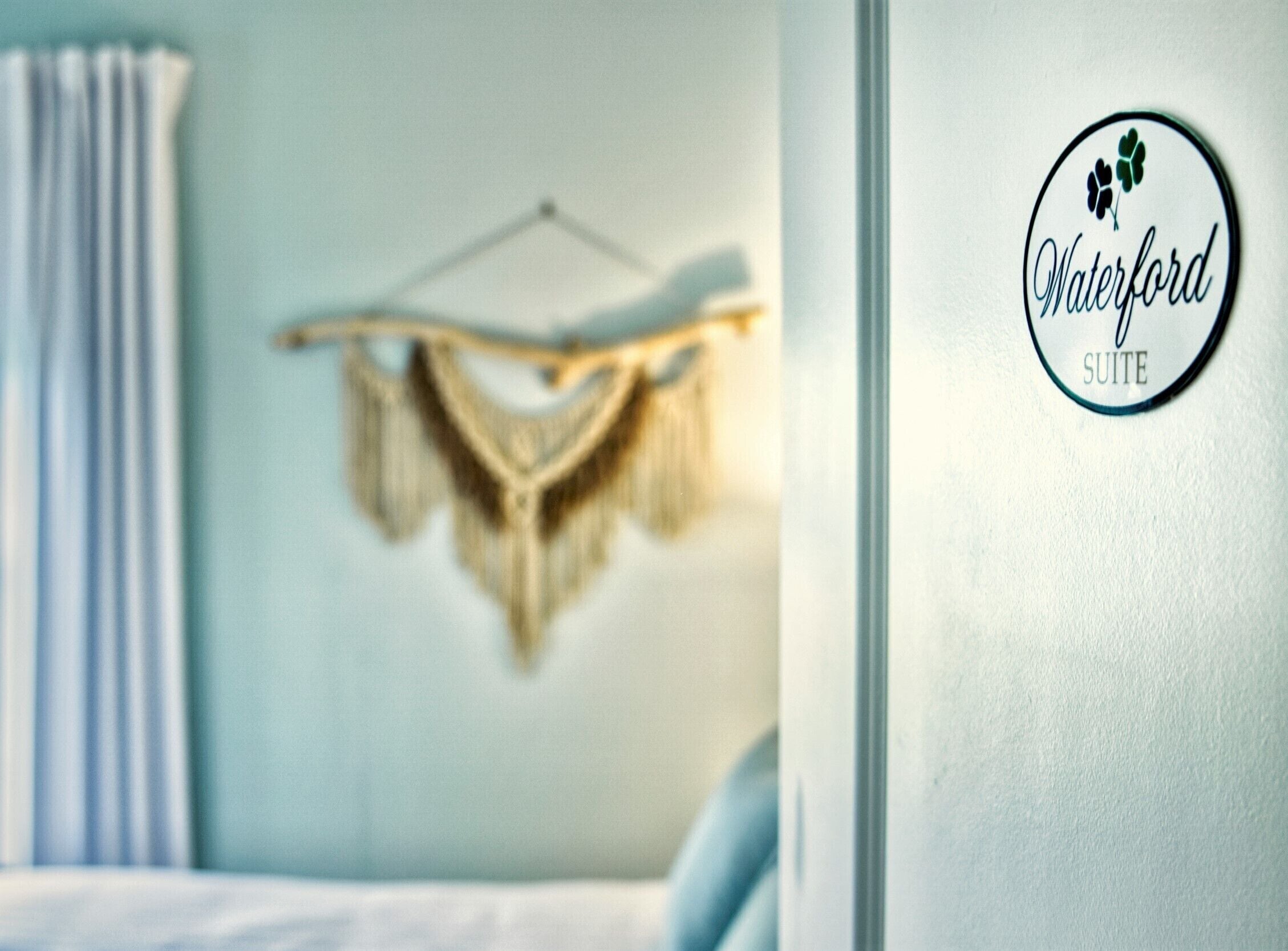A room with a bed, a hanging macrame piece, and a sign for 'Waterford SUITE'.