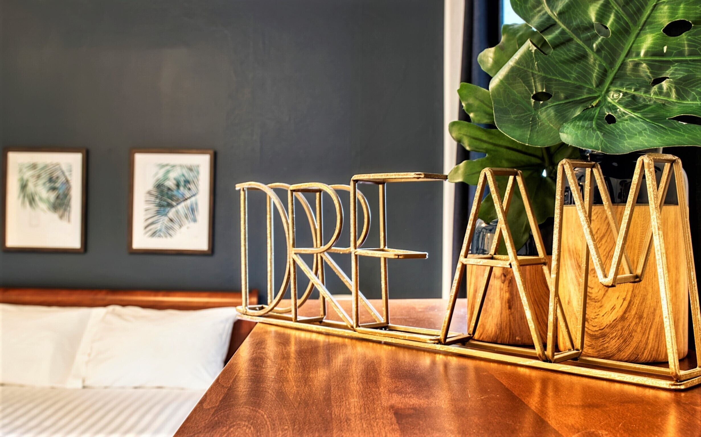A bed with white linens, a wooden nightstand, and a decorative gold metal stand with the word "DREAM" on it.