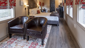 A bedroom with a bed, two leather armchairs, a desk, and a dresser. - Shamrock Suites (Florenceville-Bristol)