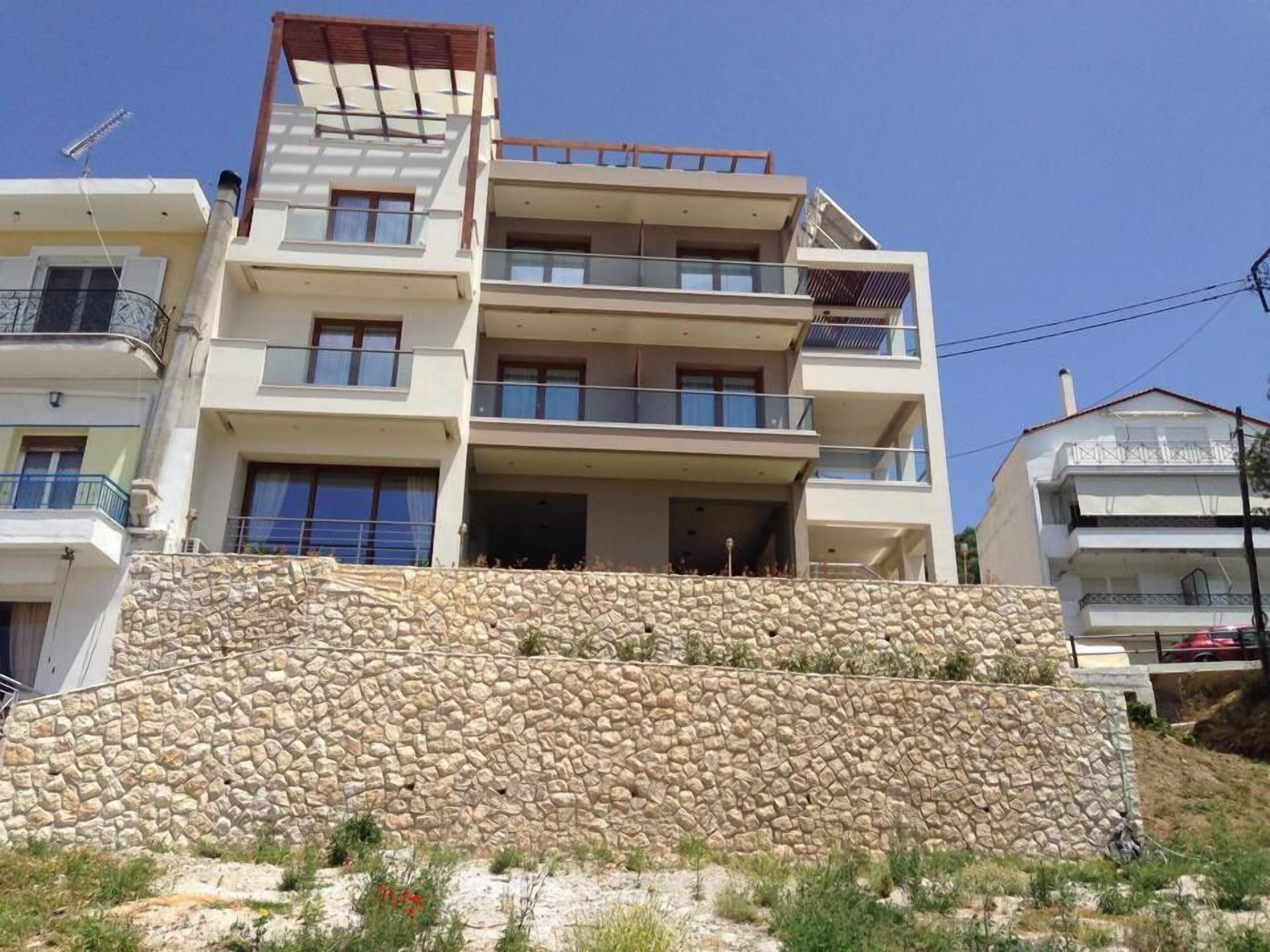Un edificio de varios pisos con balcones, un muro de piedra y cielo despejado.