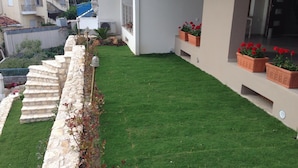 A modern building with a stone staircase, a well-maintained lawn, and potted red flowers on the balcony. - Lydia Apartments (Istiaia-Aidipsos)