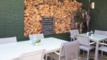 A restaurant with white tables and chairs, a stack of firewood against the wall, and a chalkboard menu.