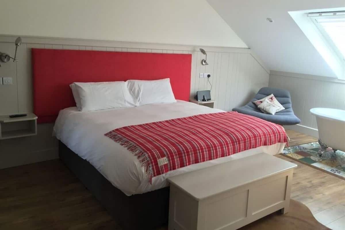 A bedroom with a large bed, a red headboard, a bedside table, a chair, a window, and a view of the sky.