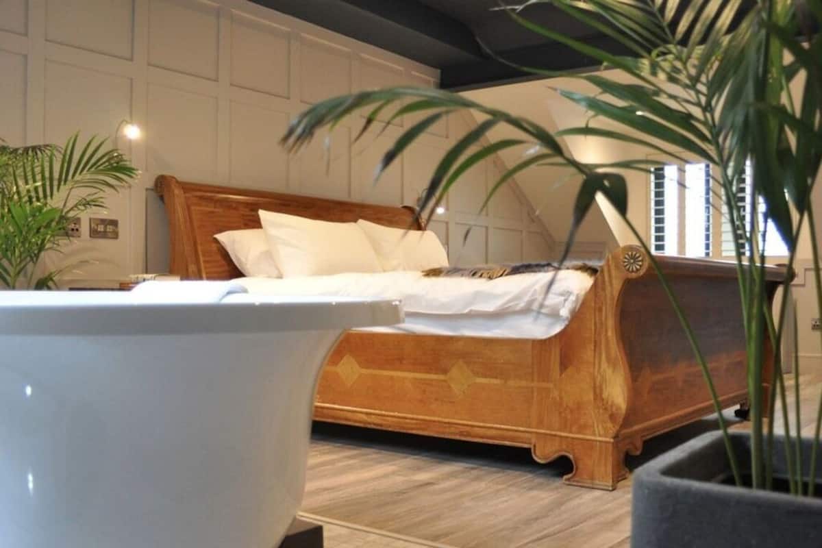 A bedroom with a wooden bed, white bedding, and a potted plant.