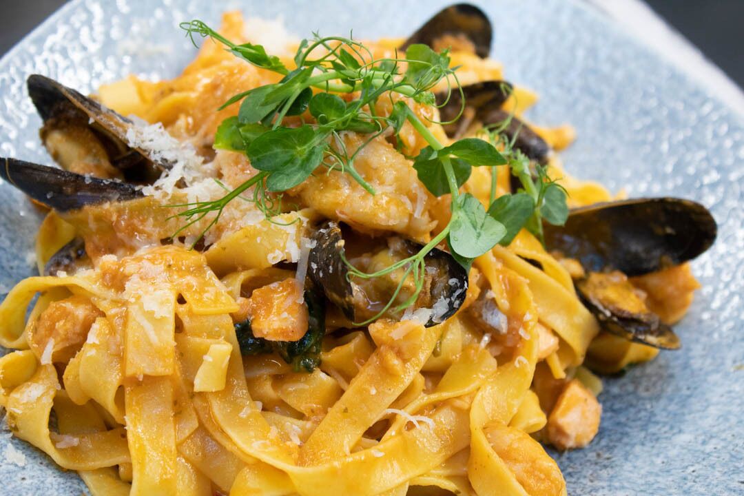 A plate of pasta with mussels and garnished with herbs.