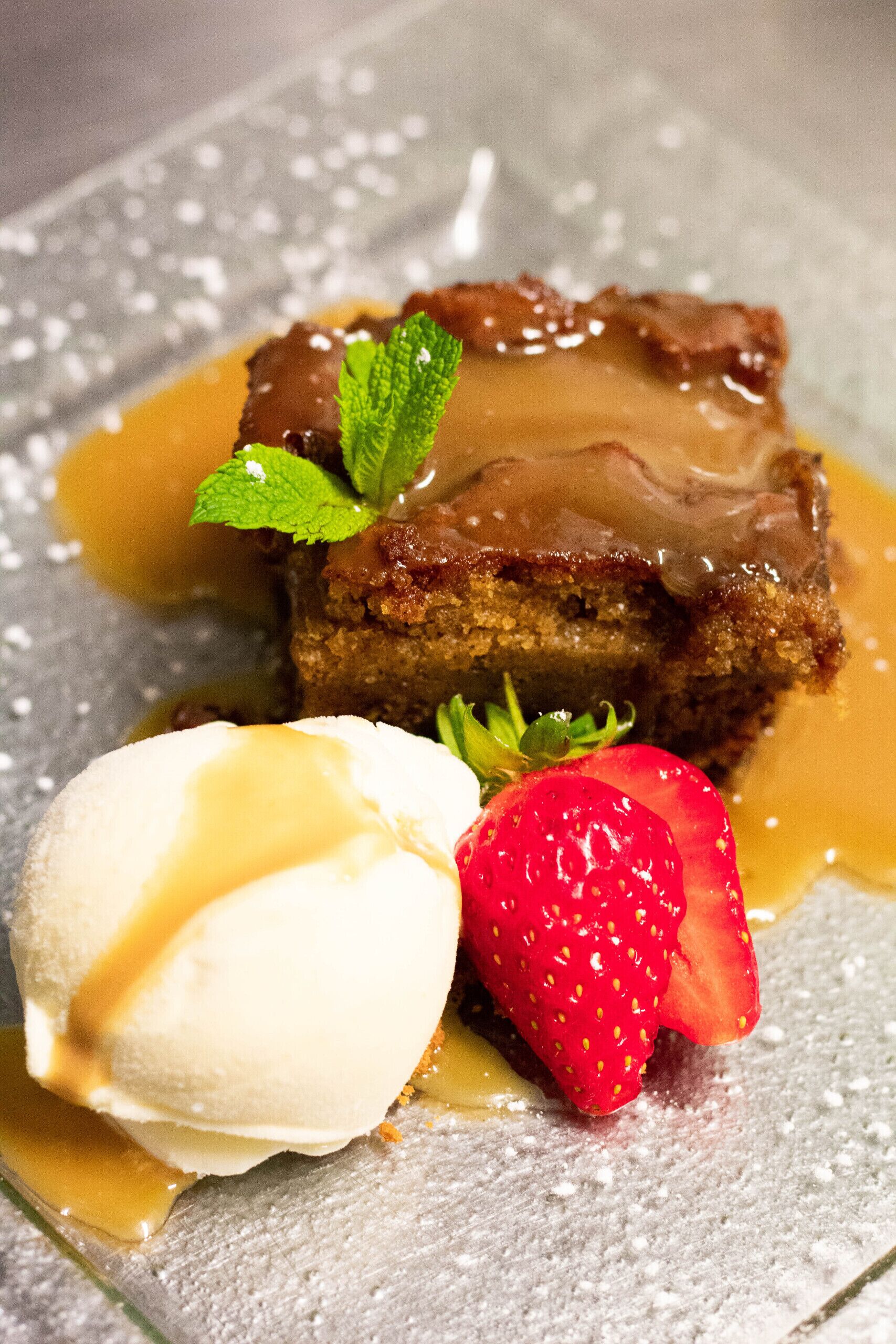 A dessert with a caramelized top, a strawberry, and a scoop of ice cream on a plate.