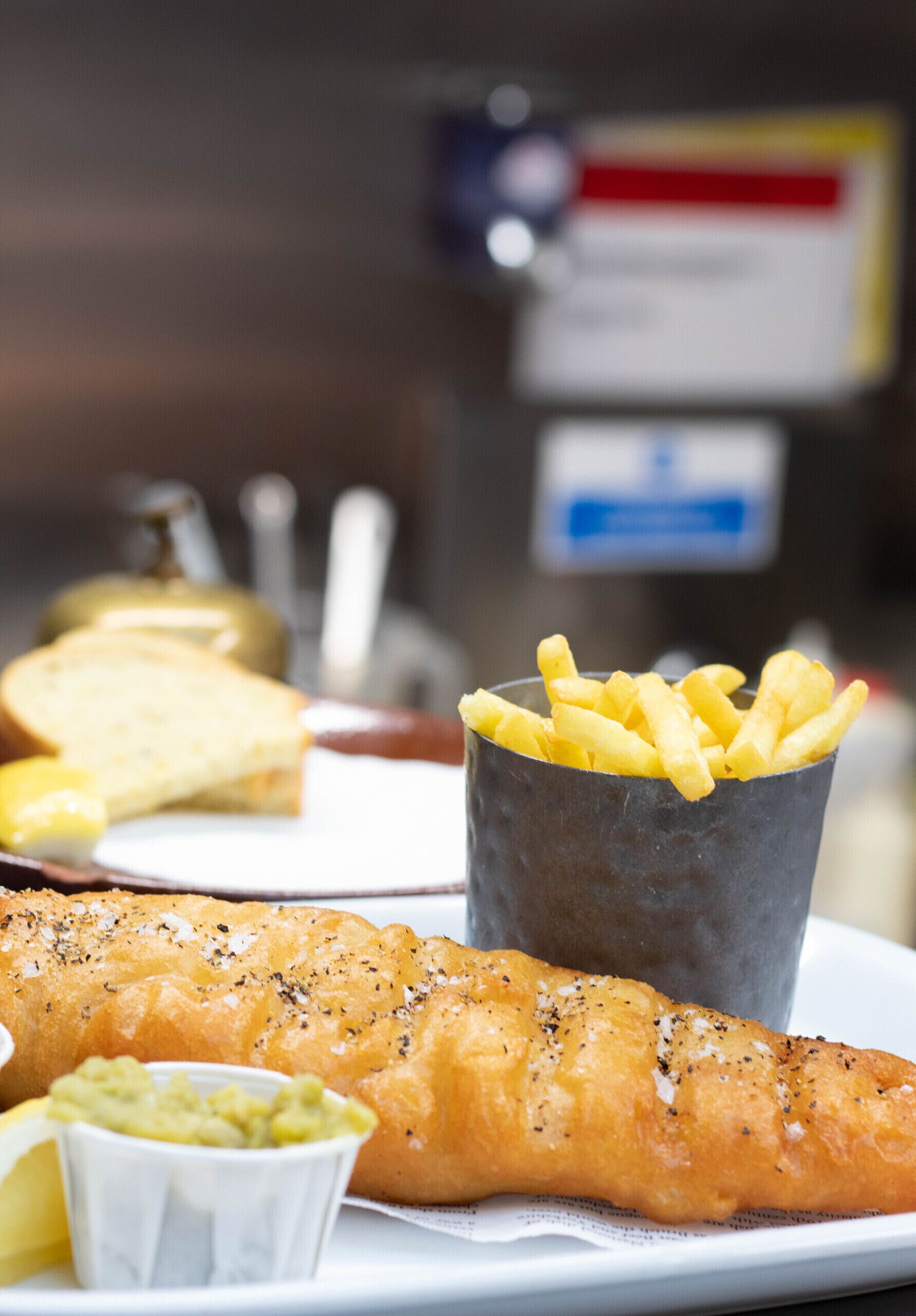 Un plato de pescado con papas fritas, un cuenco pequeño de salsa tártara y una cuña de limón.