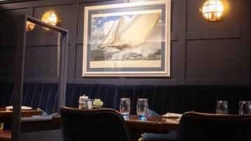 A dimly lit restaurant with a dark wood panel wall, a framed seascape painting, and a booth seating area.