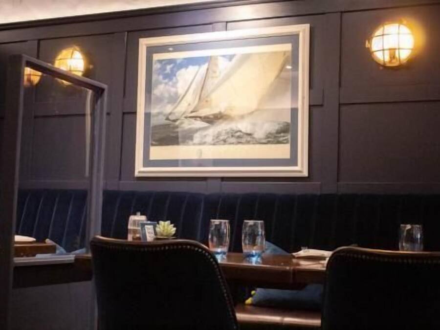 A dimly lit restaurant with a dark wood panel wall, a framed seascape painting, and a booth seating area.