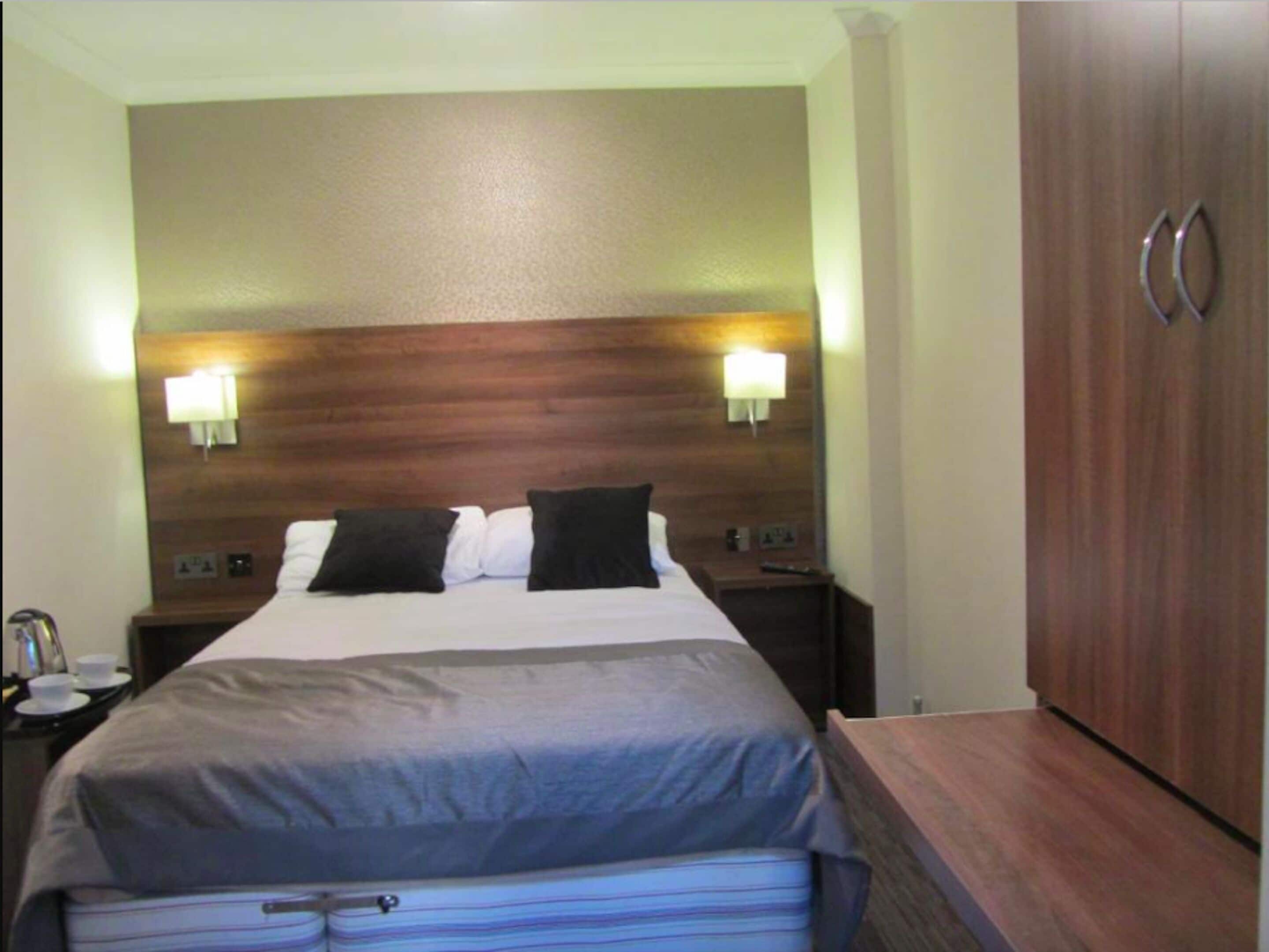 Habitación de hotel con una cama grande, dos lámparas de noche, un cabecero de madera y un armario.